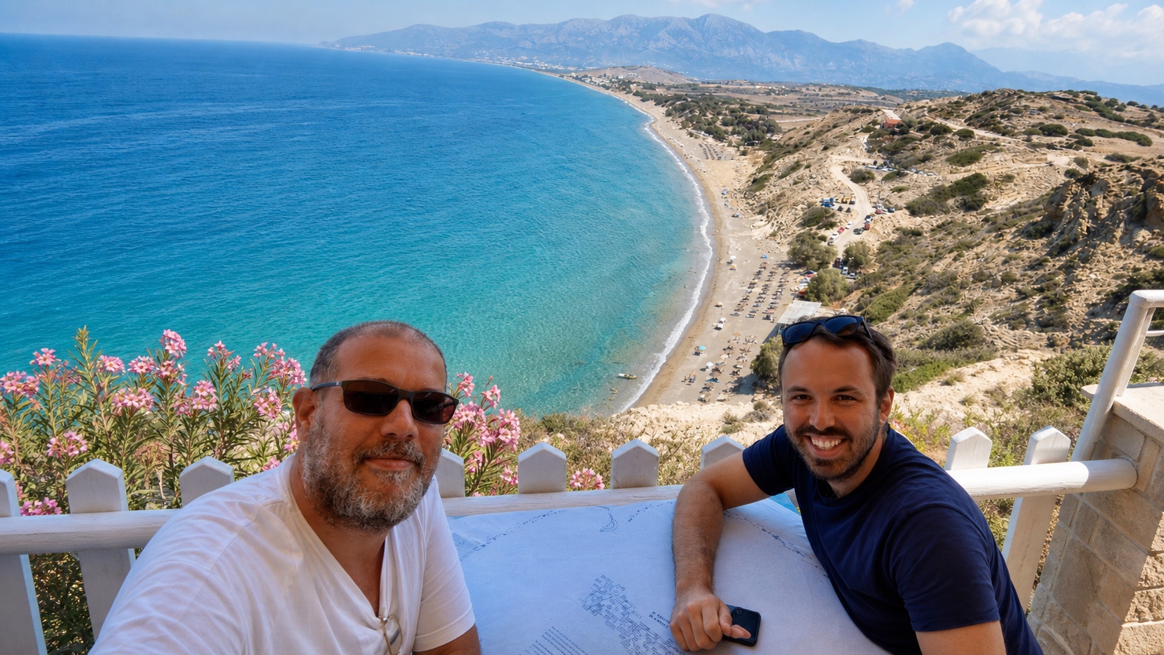 Natti and Andrew sit on a white-railed terrace above a sweeping Cretan bay.