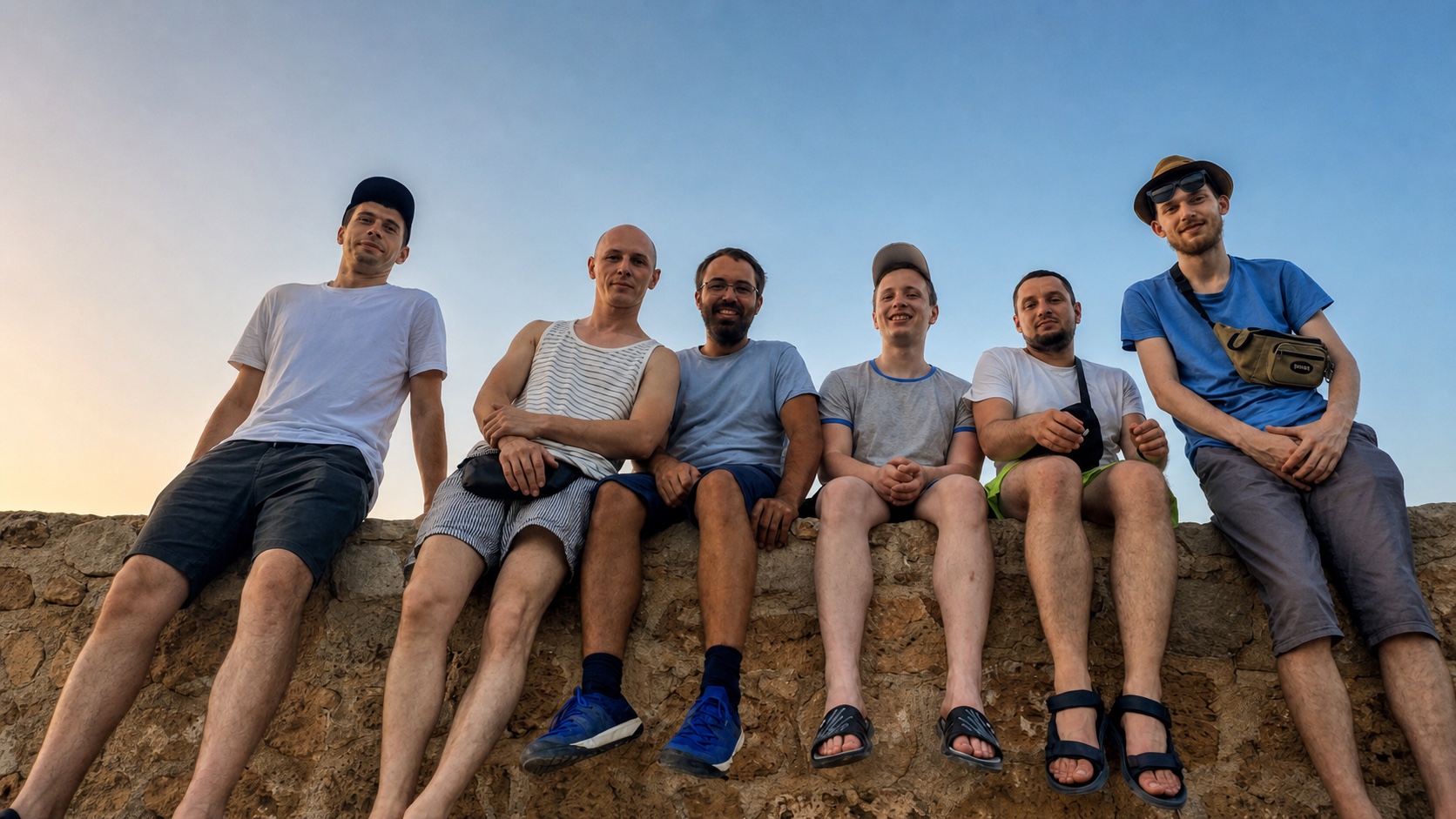 Six men sit along a stone harbor wall in Xania; Andrew is third from the left in blue shoes.